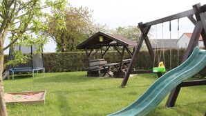 Une aire de jeux avec un toboggan, des balançoires et une table de pique-nique, le tout installé dans un espace verdoyant.