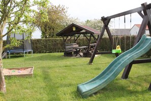Un parque infantil con tobogán, columpios y una mesa de picnic en una zona cubierta de césped.