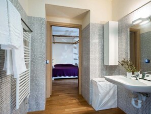 A narrow hallway leading to a bedroom with a purple bedspread, a white radiator, and a tiled wall. - Belvilla by OYO Corte Dorata (Scicli)