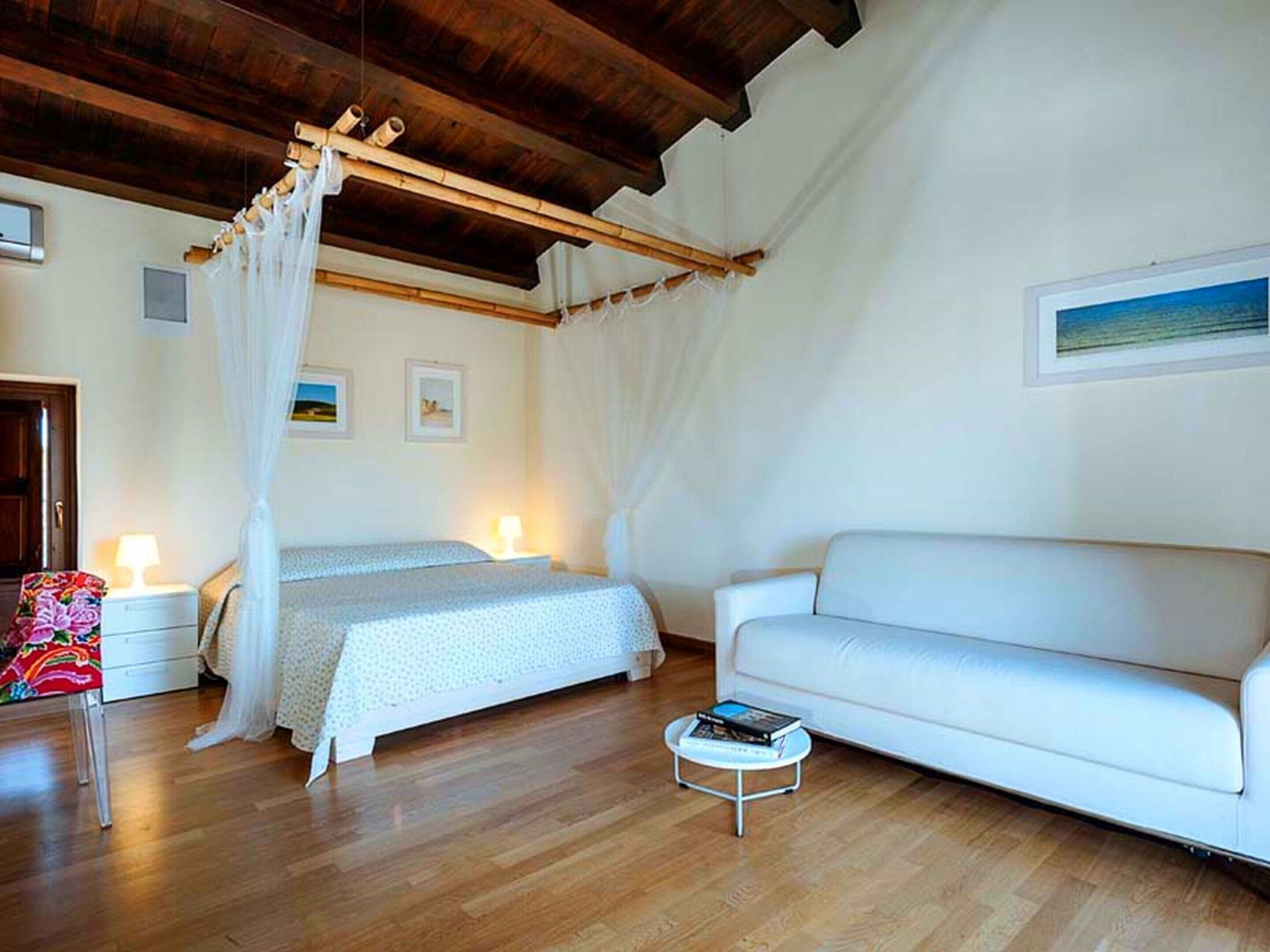 A bedroom with a canopy bed, a white sofa, and a small round table.