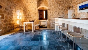A rustic stone-walled kitchen with a bar area, stone tiles, and a view through an arched doorway. - Belvilla by OYO Corte Dorata (Scicli)