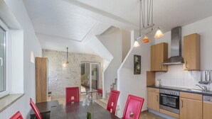 Una cocina moderna con armarios de madera, horno empotrado y comedor con mesa de madera y sillas rojas.