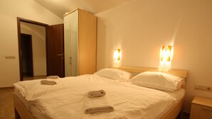 Una cama bien hecha con dos almohadas y dos toallas dobladas, un armario de madera y una mesita de noche con una lámpara.