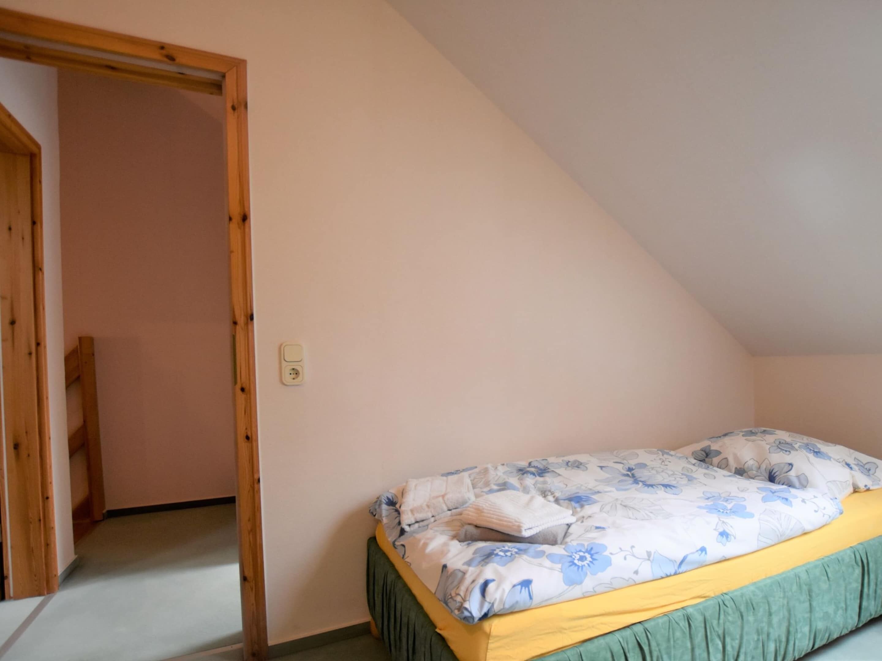 A bedroom with a single bed, a wooden door, and a light switch on the wall.