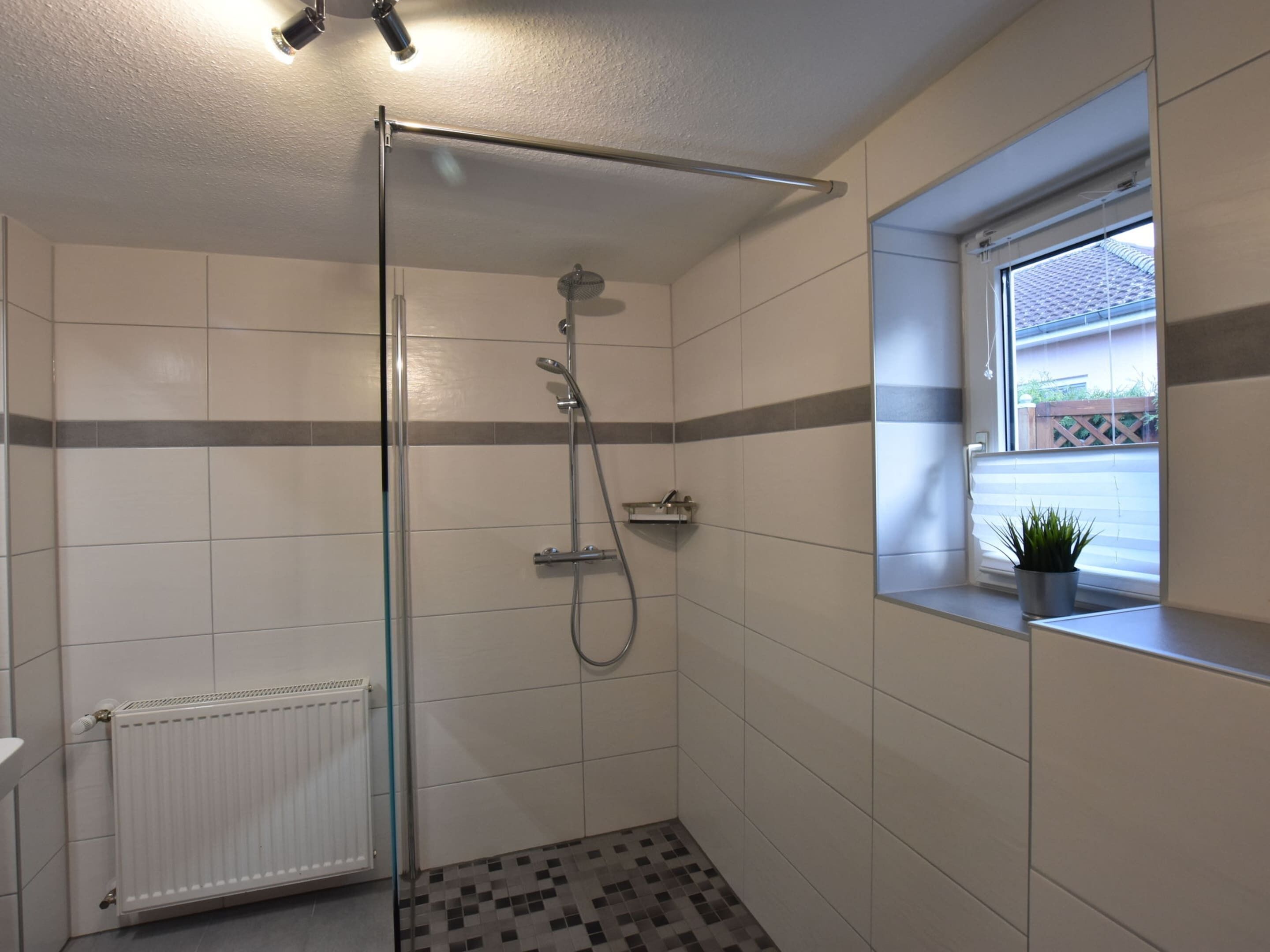 A modern bathroom with a glass shower enclosure, a white radiator, and a window with a view of the outside.