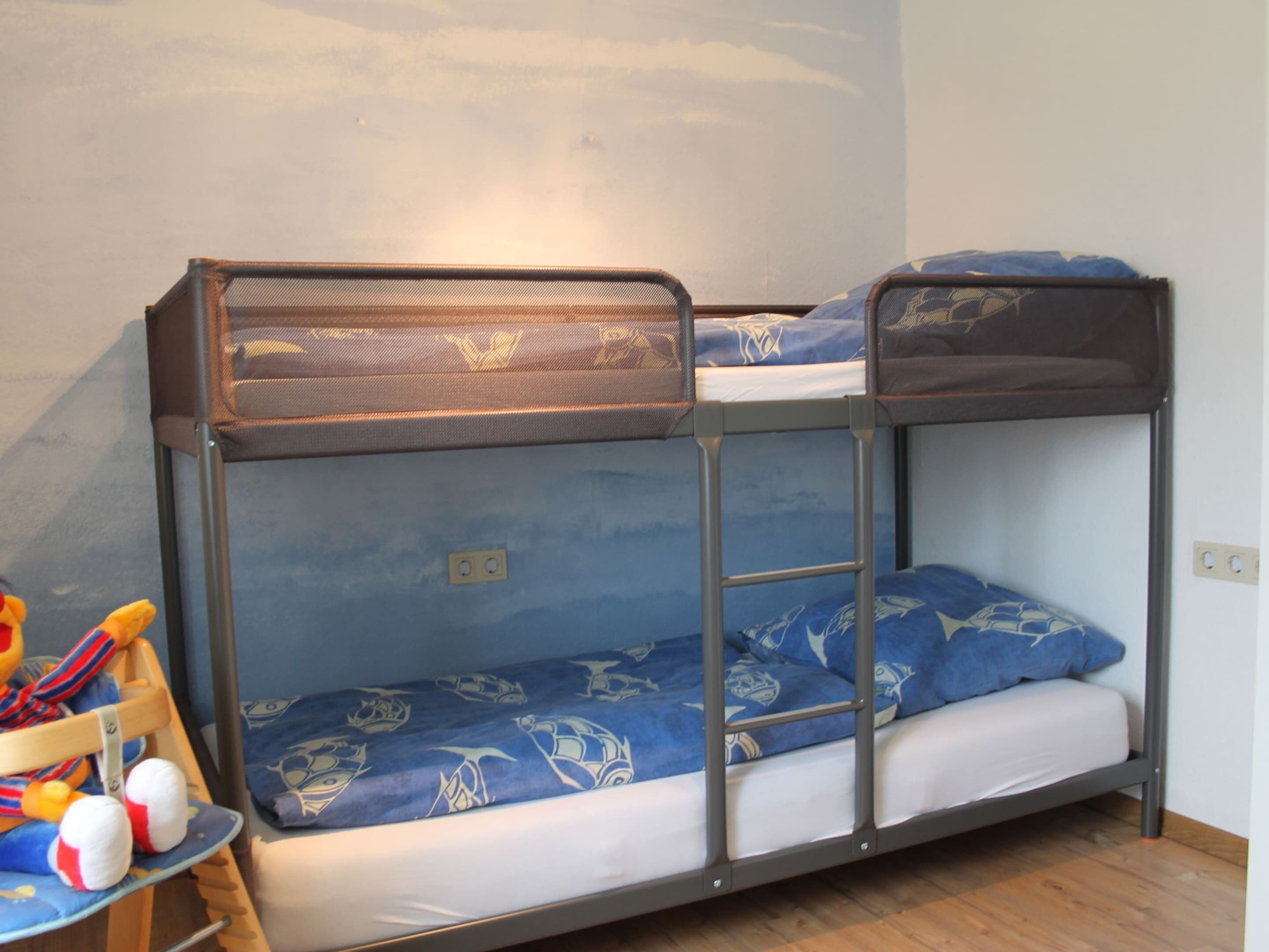 A bunk bed with a mesh top and a lower bunk with a patterned blue mattress.