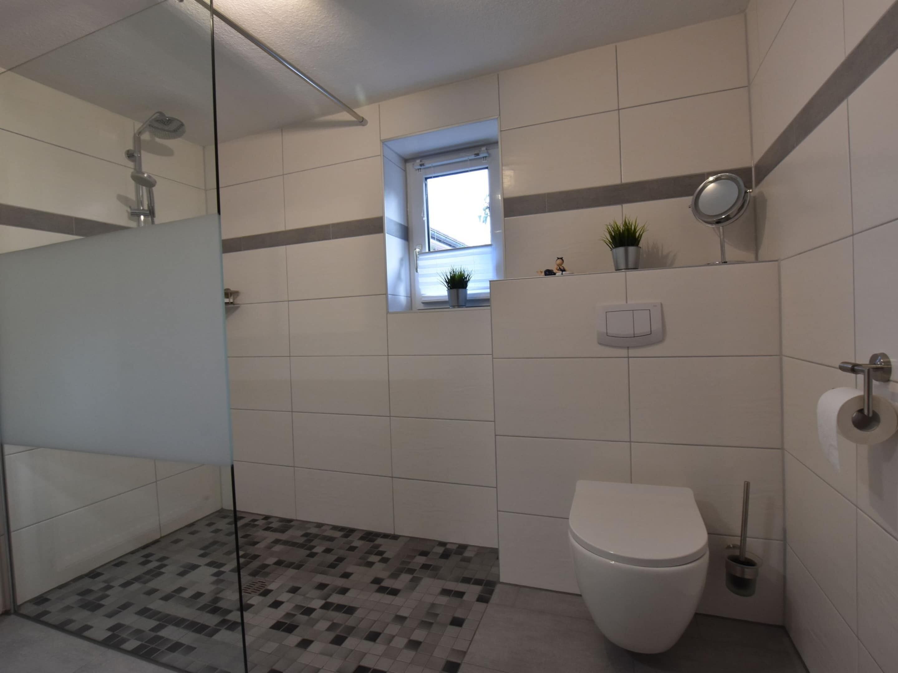 Ein modernes Badezimmer mit Dusche, Toilette und einem kleinen Fenster.
