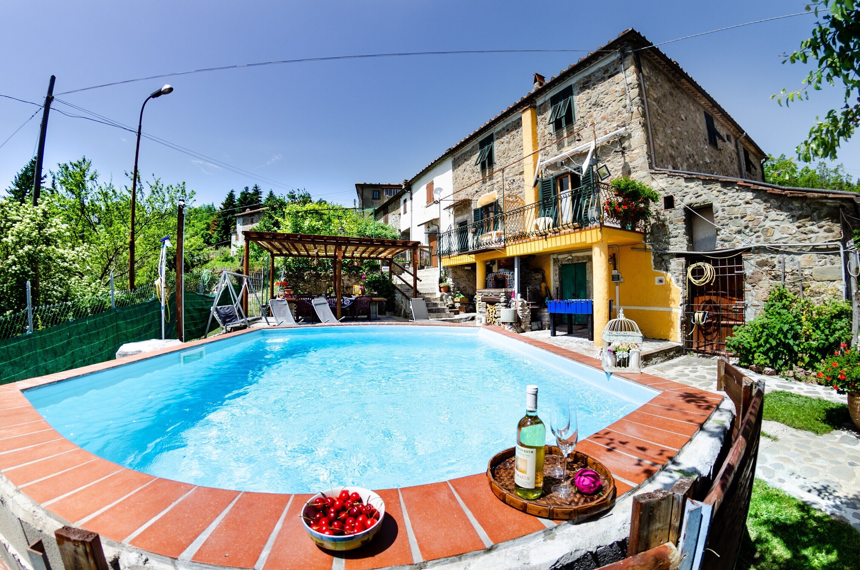 A swimming pool with a tiled edge, a wooden deck, and a table with a bottle and glass.