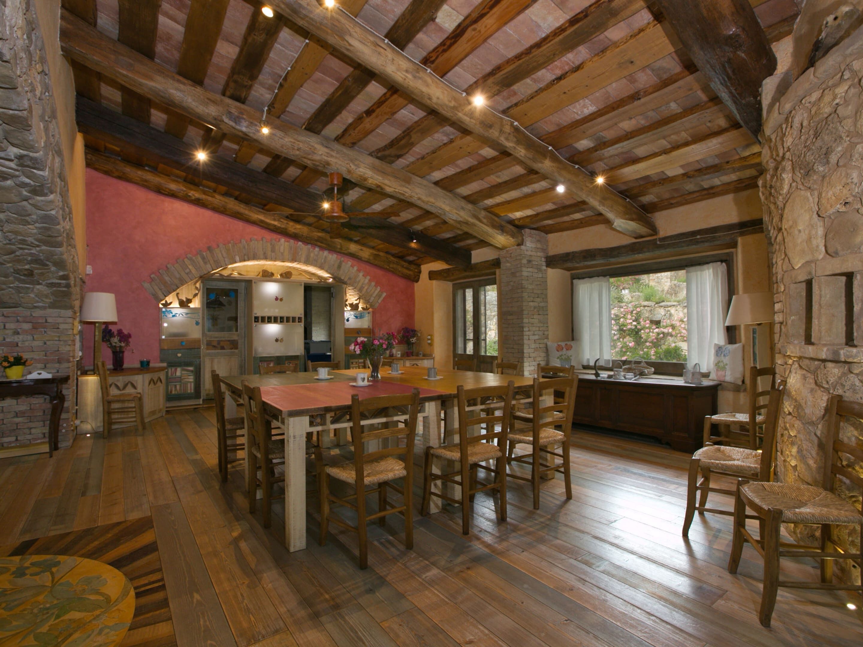Ein rustikales Interieur mit sichtbaren Holzbalken, einer Steinwand und einem Holzesstisch mit Stühlen.
