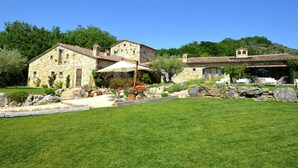A stone house with a patio area, surrounded by a well-maintained lawn and trees. - Villa Solace - Comfort Charm (Guardea)