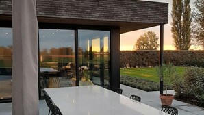 Ett modernt utomhusområde för måltider, inrymt i en glasstruktur, med ett bord, stolar och en krukväxt.