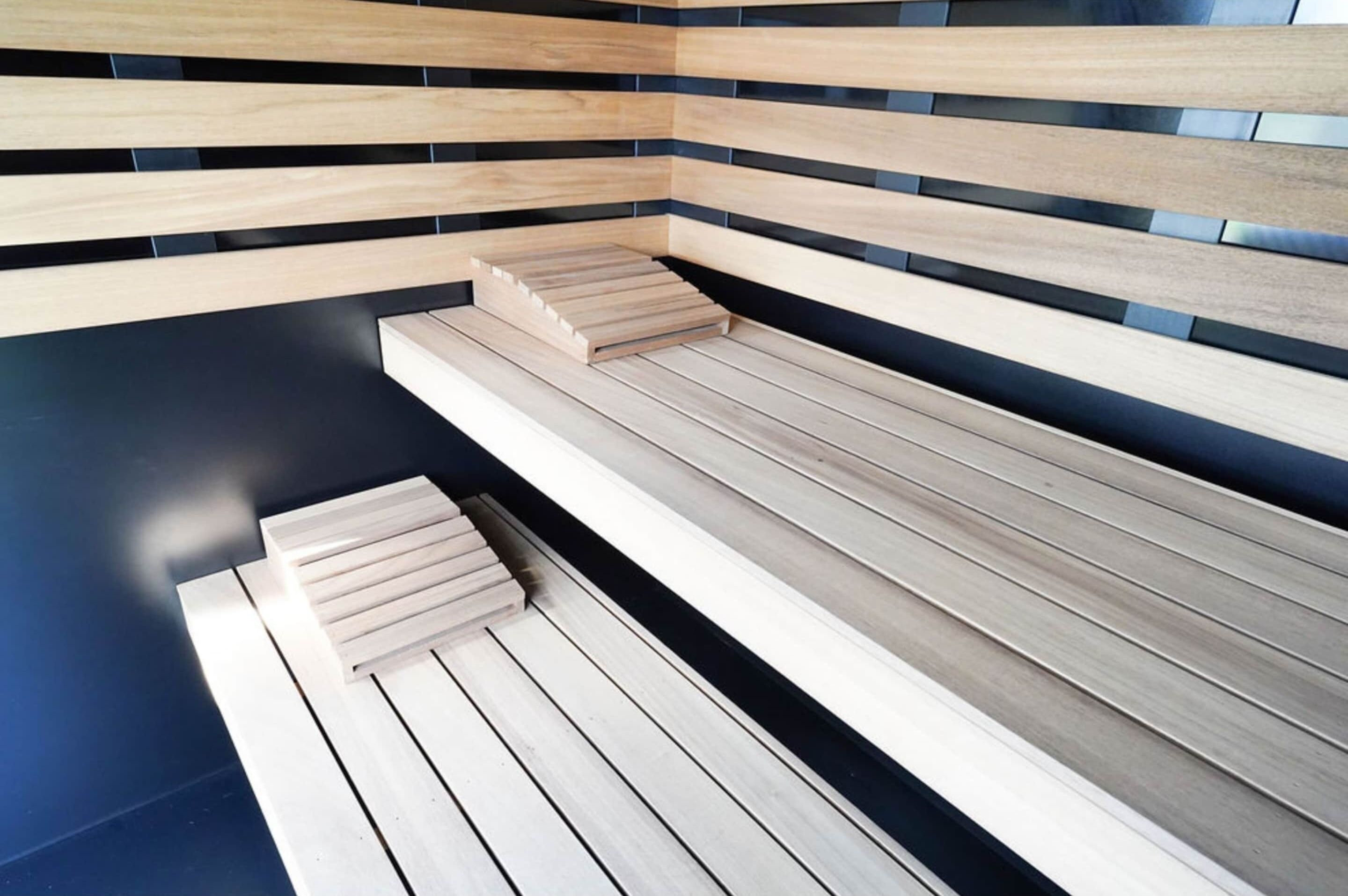 A modern sauna with wooden benches and black-tiled walls.