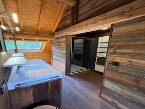 A wooden cabin interior with a bathroom featuring a sink and mirror, a skylight, and a door leading to a dark room. - Chalet in Ovifat Near Ski Slopes (Waimes)