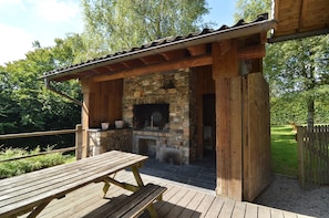 A rustic outdoor patio with a stone fireplace, wooden benches, and a wooden pergola. - Chalet in Ovifat Near Ski Slopes (Waimes)