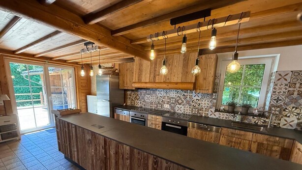 A modern kitchen with wooden cabinets, a large island, and pendant lighting. - Chalet in Ovifat Near Ski Slopes (Waimes)