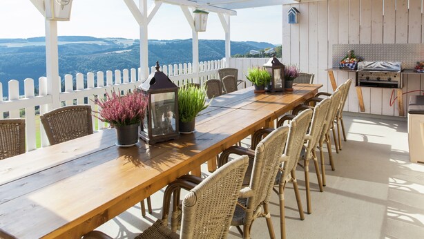 An outdoor dining area with a wooden table and wicker chairs, a grill, and potted plants. - Beautiful Holidayhome With Sauna and Terrace (Harscheid)