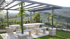 Une terrasse extérieure agrémentée d’une pergola, de bancs en pierre et offrant une vue sur des collines ondoyantes.
