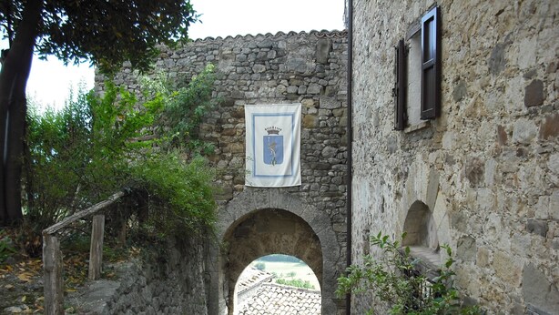 Un arc en pierre mène à une cour intérieure, avec un bâtiment à toit de tuiles en arrière-plan.