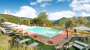A swimming pool surrounded by lounge chairs and umbrellas, set against a backdrop of hills and a clear sky. - Rustic Serenity Farmhouse (Monte Santa Maria Tiberina)