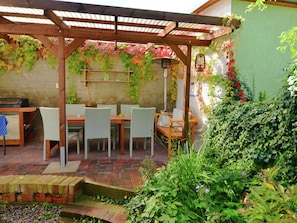 A covered patio with a table and chairs, surrounded by greenery and a brick pathway. - Cozy Holiday Home in Kappe With Balcony (Zehdenick)
