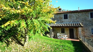 A stone building with a tiled roof, a small patio with outdoor furniture, and a tree with yellow leaves. - Holiday Home in Dicomano (Dicomano)