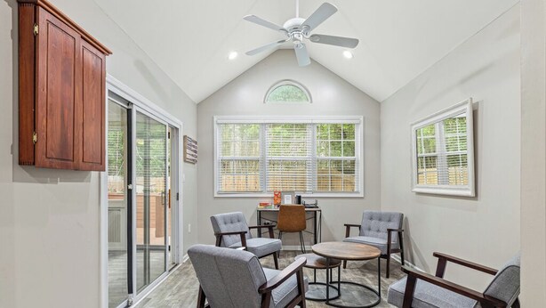 Une véranda avec un ventilateur de plafond, de grandes fenêtres et un coin repas comprenant des chaises et une table.
