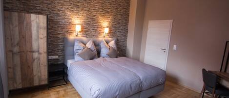 A bedroom with a bed, wooden wardrobe, and a stone wall.