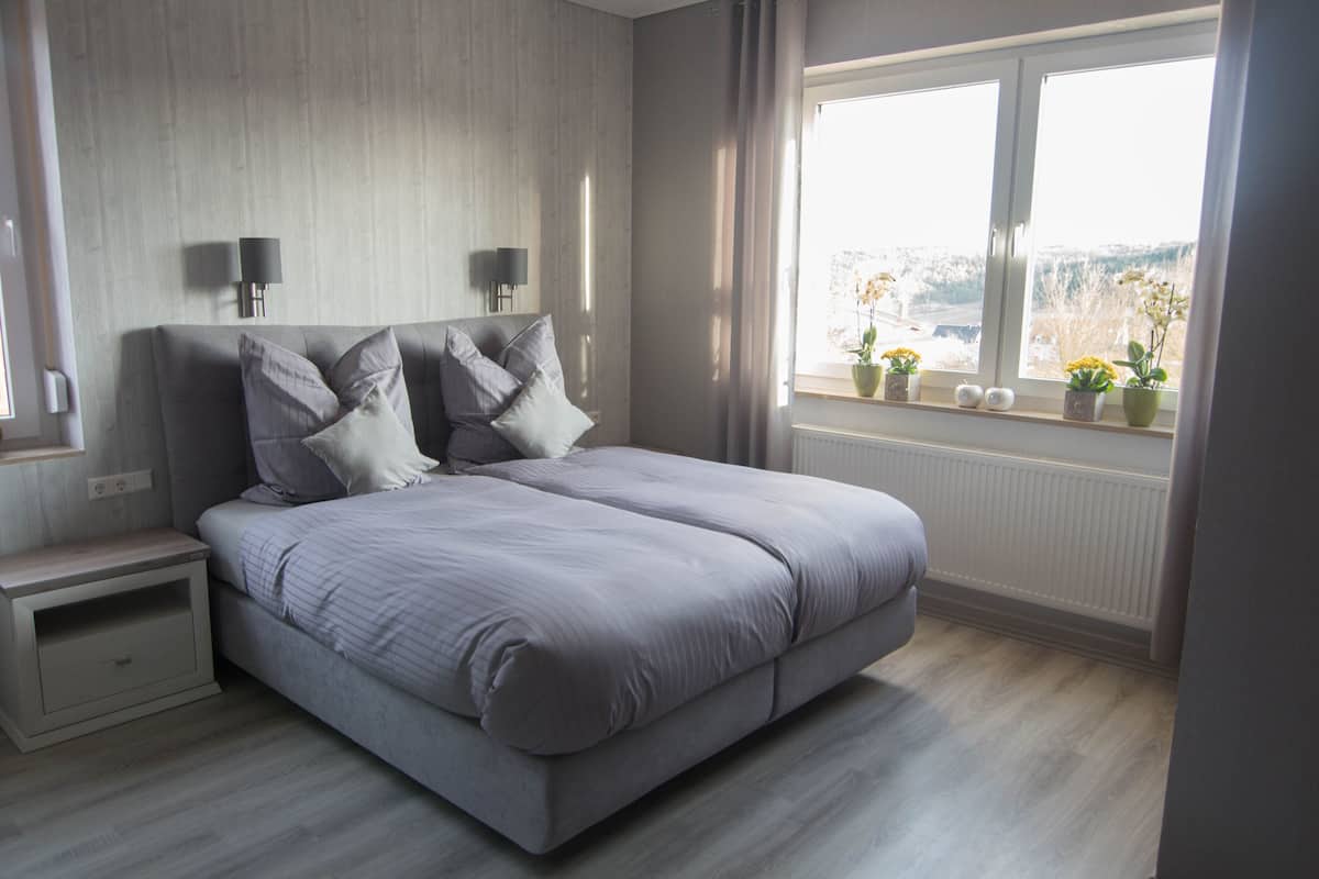 Une chambre moderne avec un grand lit, des lampes de chevet, une table de nuit et une fenêtre donnant sur l’extérieur.