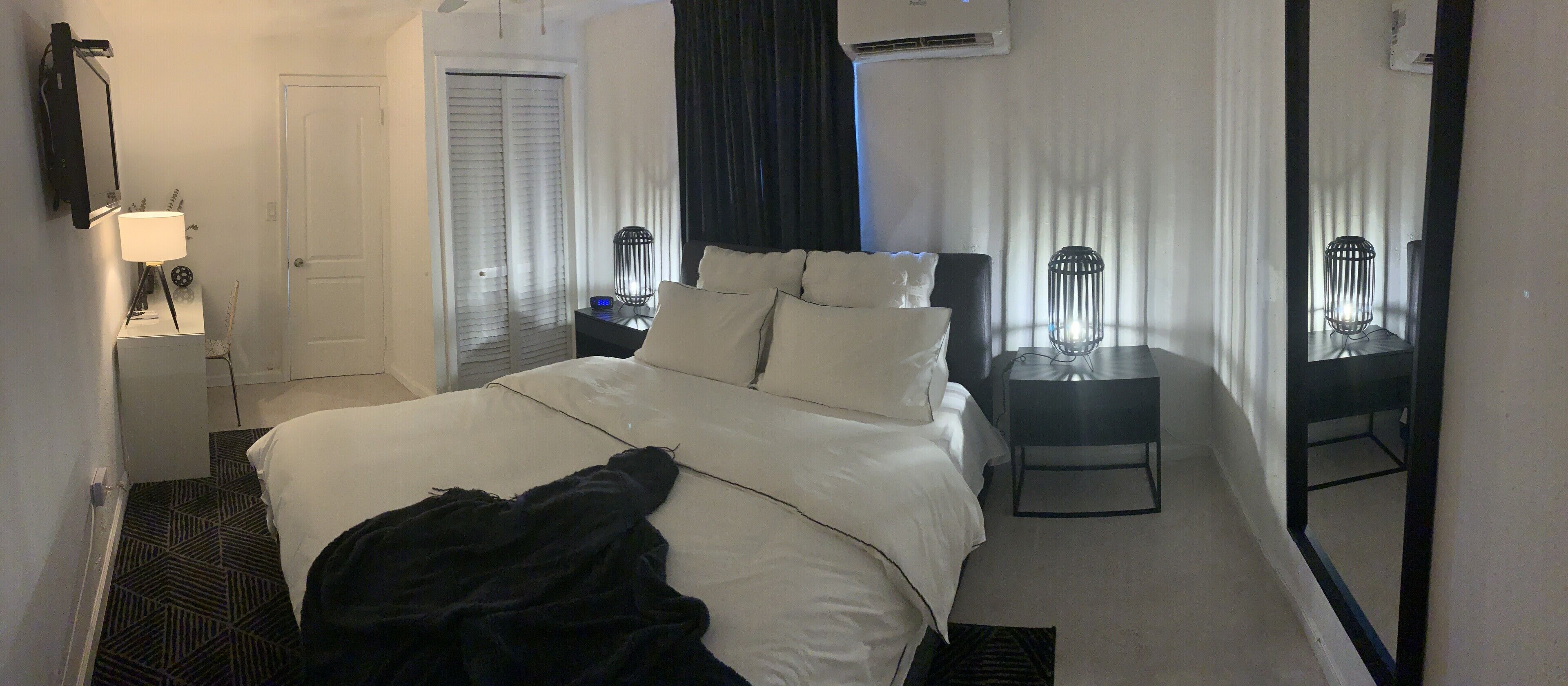 Une chambre d’hôtel comprenant un lit, une table de chevet, une lampe, un appareil de climatisation et un miroir.