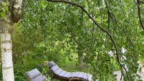 Dos sillones de madera con cojines grises en un jardín verde y exuberante.