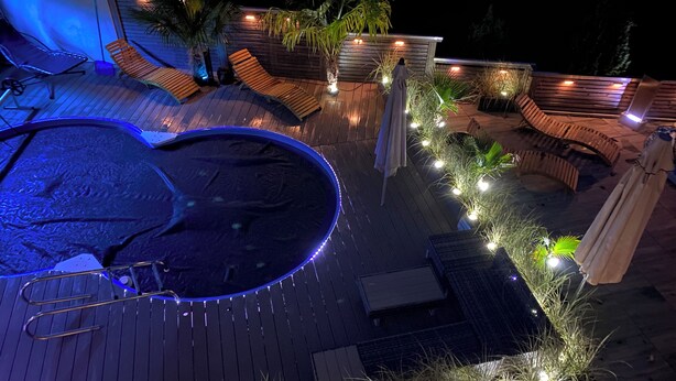 Un área de piscina en la azotea con hidromasaje, sillas de descanso e iluminación con guirnaldas.