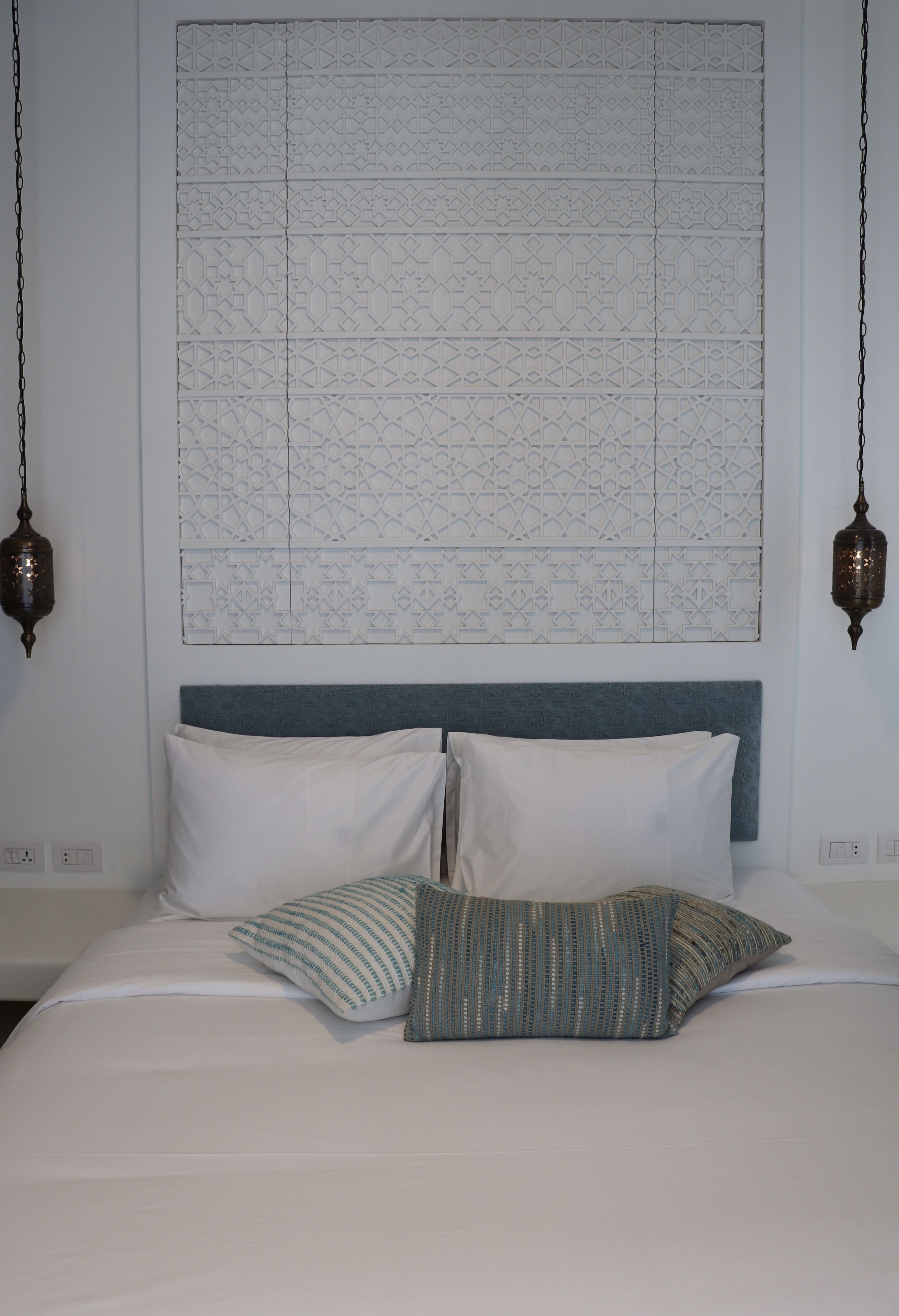 A neatly made bed with white linens and two pillows, a blue headboard, and a decorative wall hanging above.