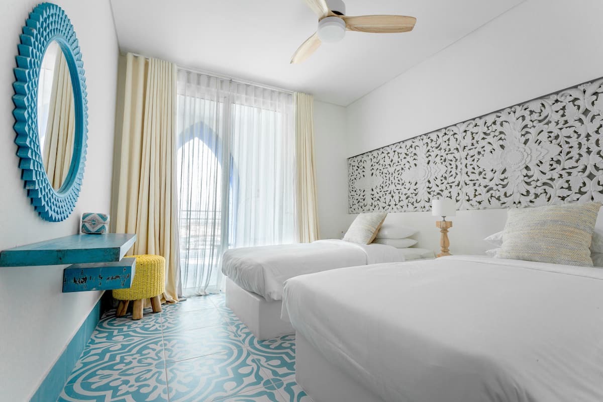 A hotel room with two beds, a ceiling fan, a decorative mirror, and a patterned floor.