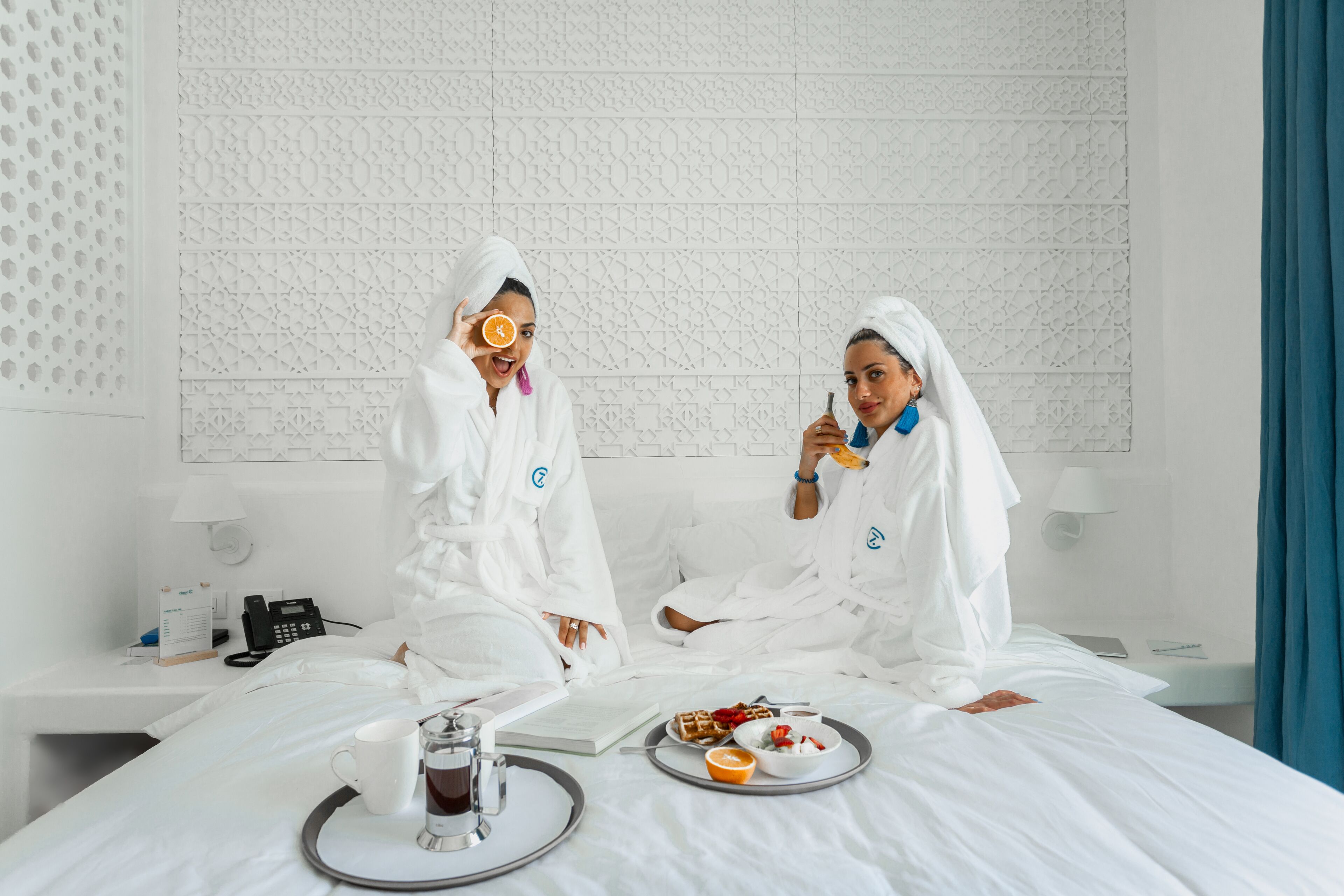 Ein Hotelzimmer mit einem Bett, einem Nachttisch mit Telefon, einer Lampe und einem Tablett mit Frühstücksgegenständen.