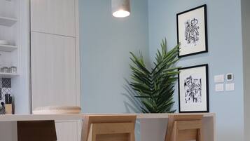 A modern kitchen with white cabinets, wooden bar stools, pendant lights, and framed artwork on the wall.