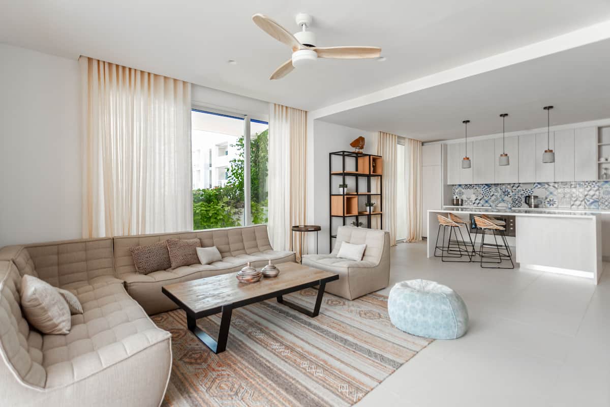 A modern living room with a sofa, coffee table, and ottoman. There is a kitchen area with bar stools and a dining table.