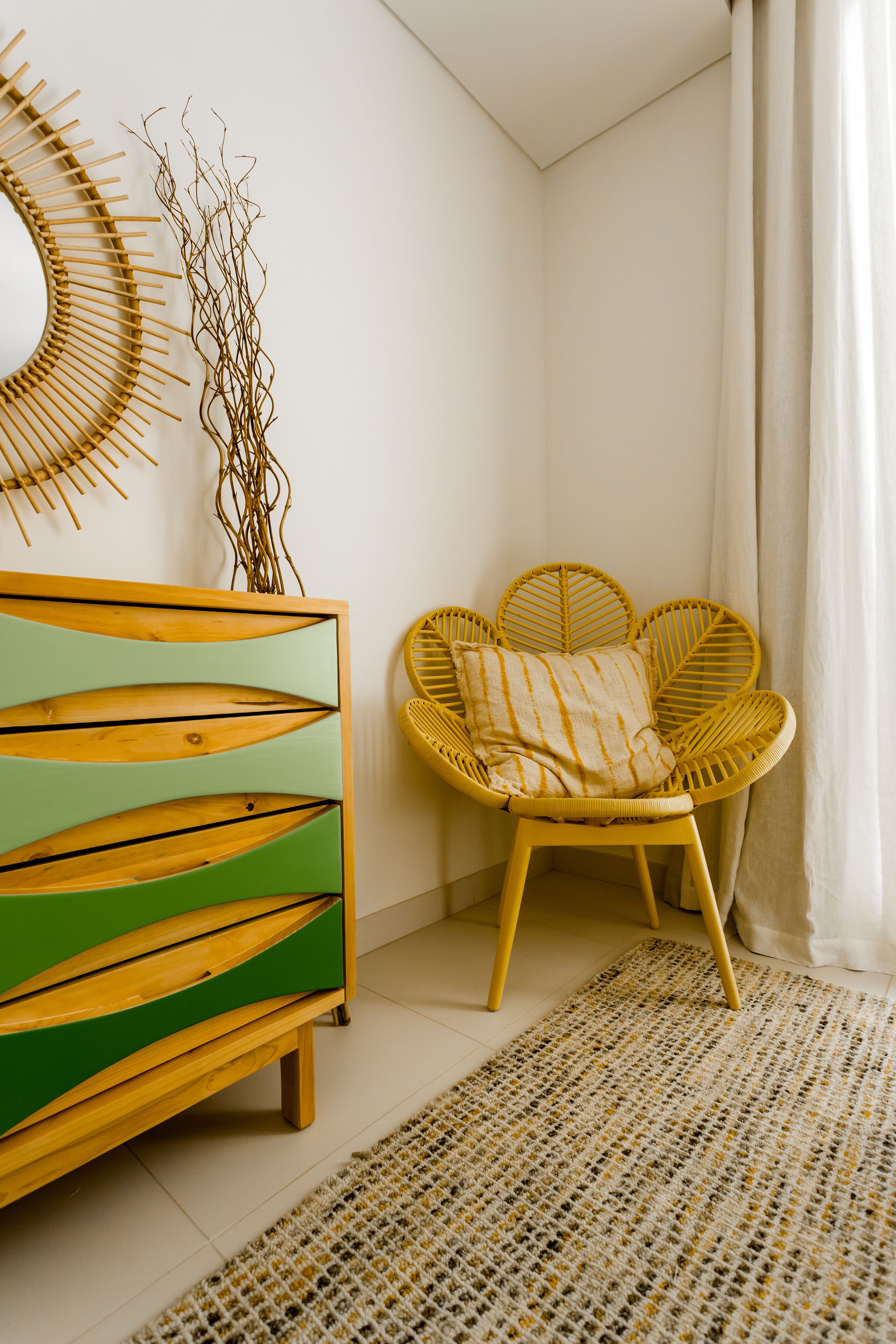 Una habitación de esquina con un armario de madera, un sillón de mimbre y un tapete tejido.