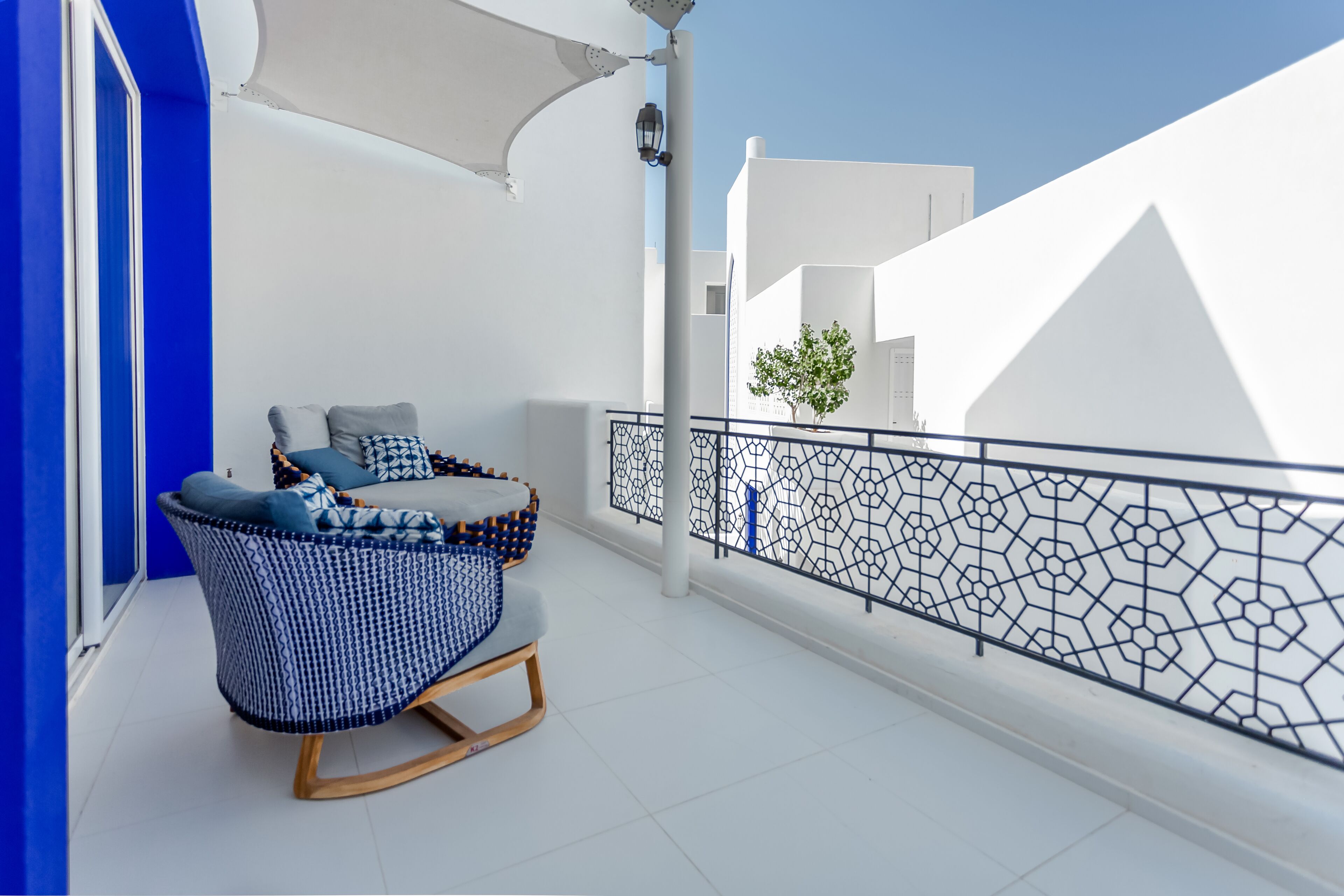 A balcony with a blue and white chair, a white railing, and a view of a white building.