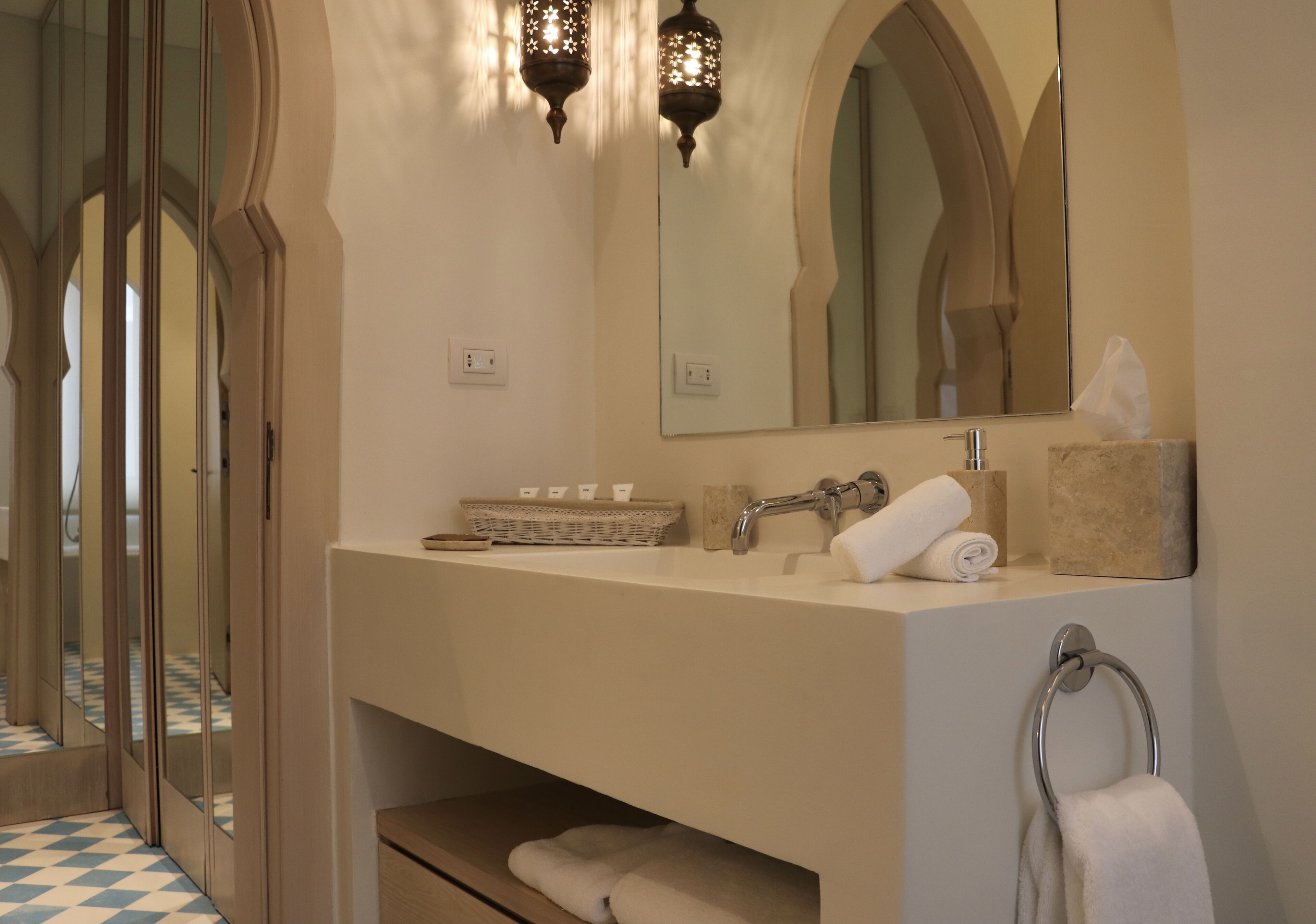 A bathroom with a large mirror, two wall-mounted lights, a sink, and a towel rack.