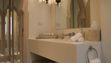 A bathroom with a large mirror, two wall-mounted lights, a sink, and a towel rack.