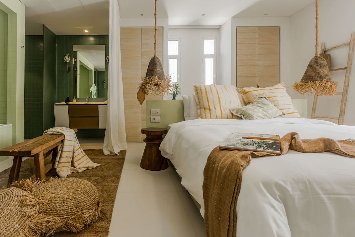 A bedroom with a large bed, a wooden bench, a bedside table, and a hanging light fixture.