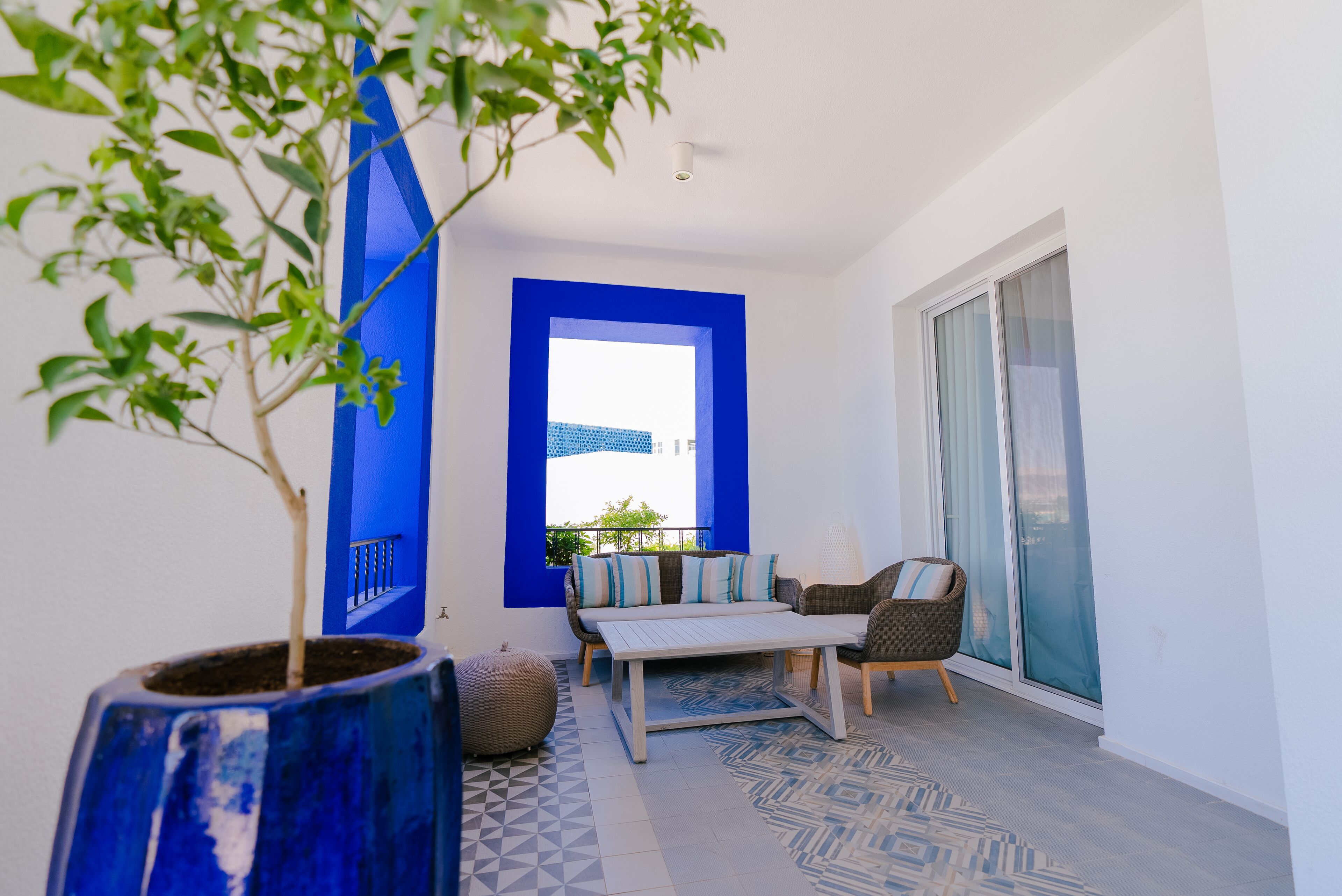 Un balcón con una ventana de marco azul, un sofá, una mesa y una silla.
