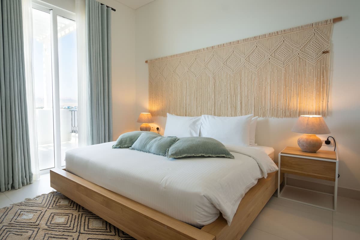 A modern bedroom with a large bed, a macrame wall hanging, and a view of the outdoors.