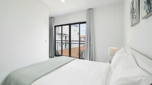 A modern hotel room with a large bed, a view of buildings through a window, and a nightstand with a lamp. - In the Funchal city center, Santa Luzia I (Funchal)
