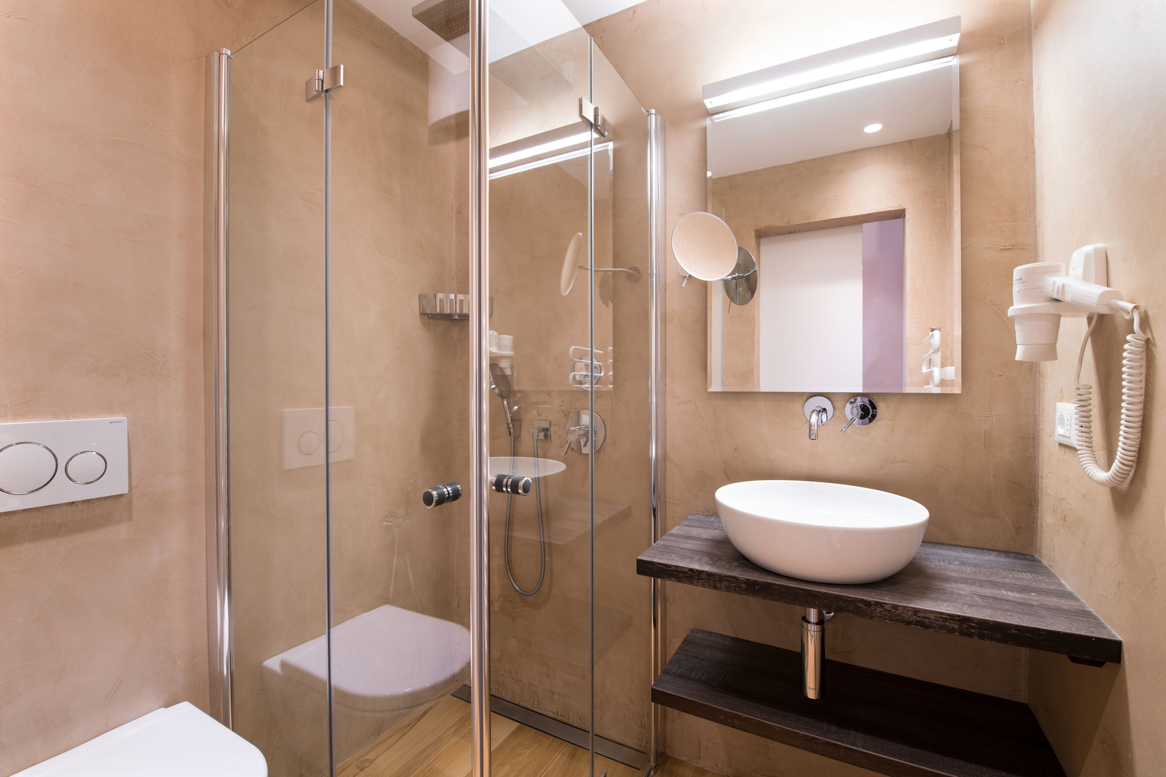 Un baño moderno con ducha de vidrio, un lavamanos blanco y un espejo sobre él.
