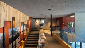 Un interior moderno con una escalera de madera, barandilla de cristal y una pared con cuadros enmarcados.