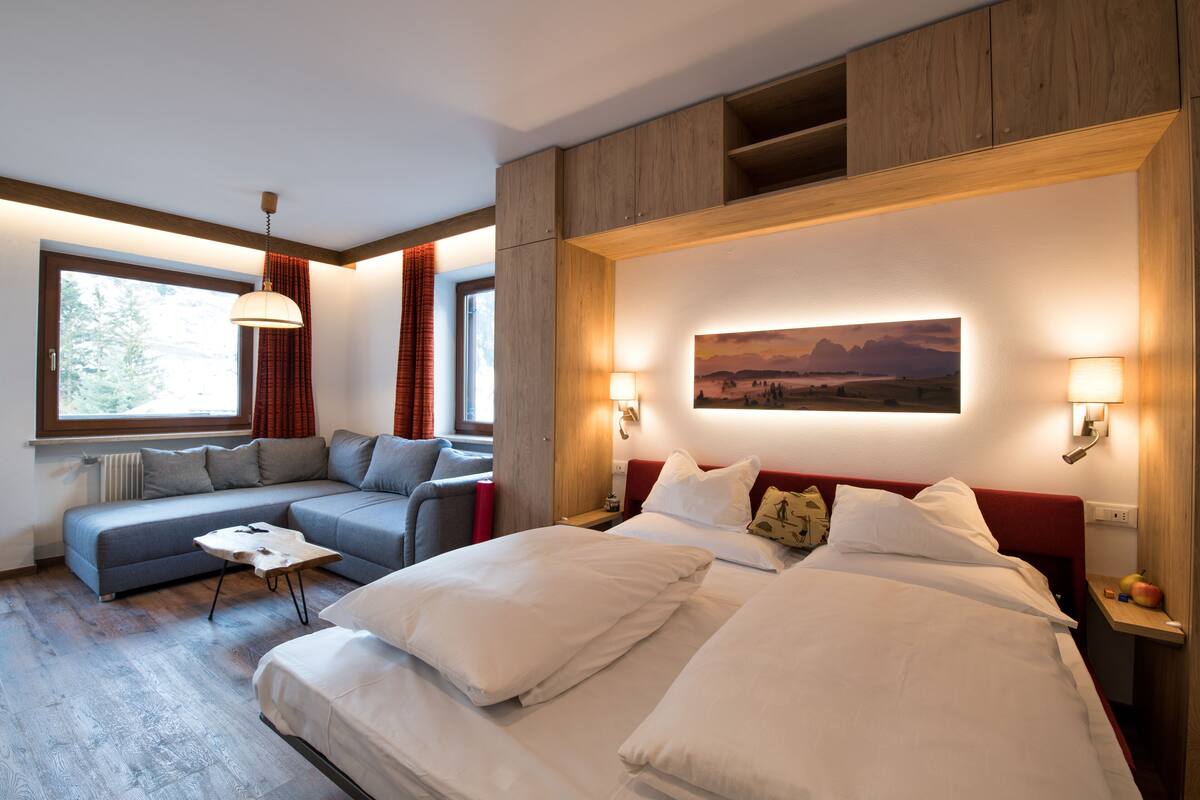 A modern hotel room with a large bed, a sofa, a small table, and a painting on the wall.