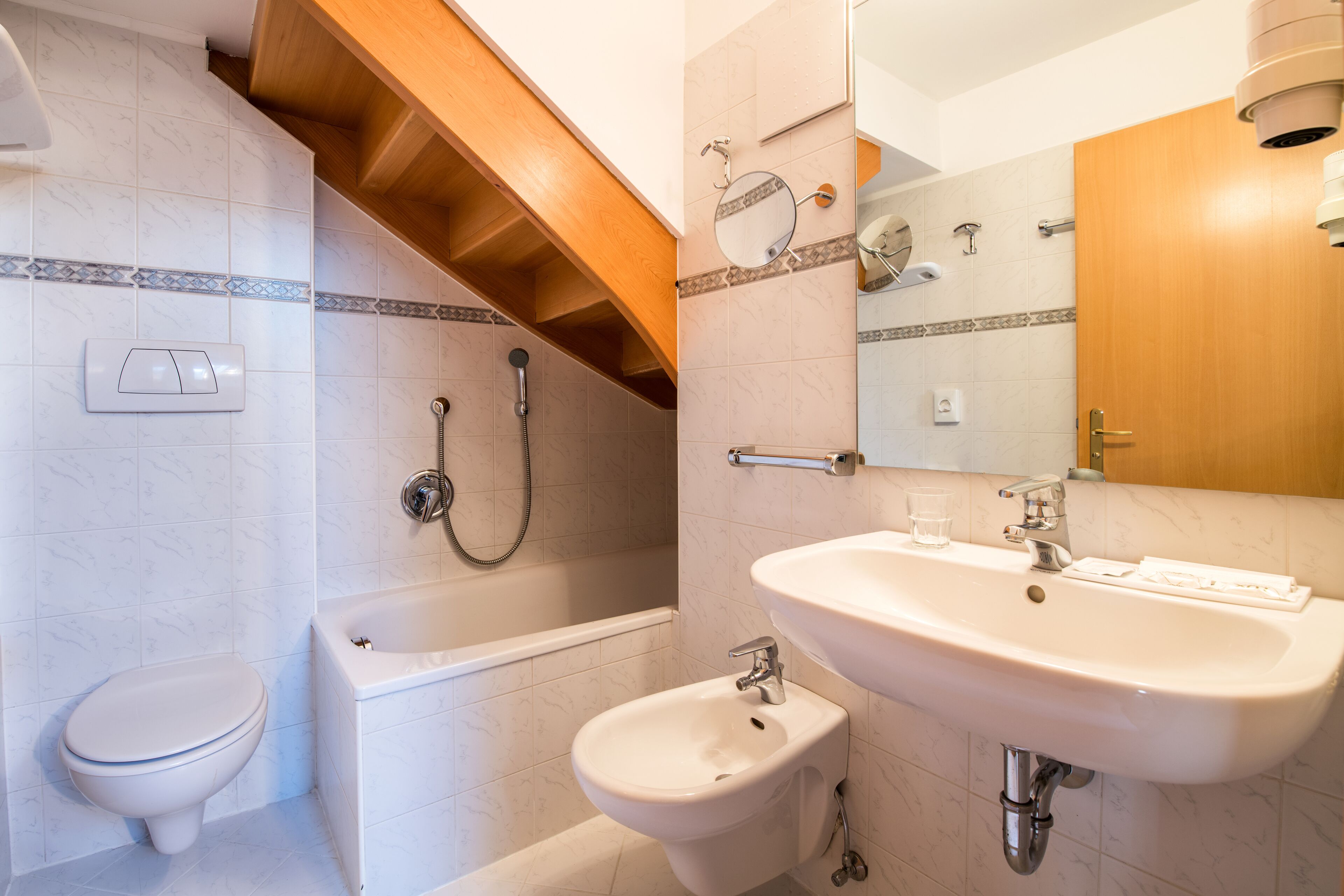 A bathroom with a toilet, bathtub, bidet, sink, and mirror.
