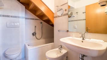 A bathroom with a toilet, bathtub, bidet, sink, and mirror.