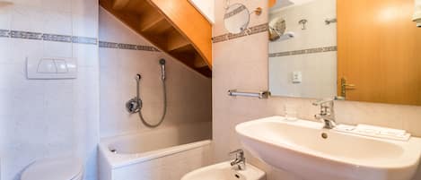 A bathroom with a toilet, bathtub, bidet, sink, and mirror.